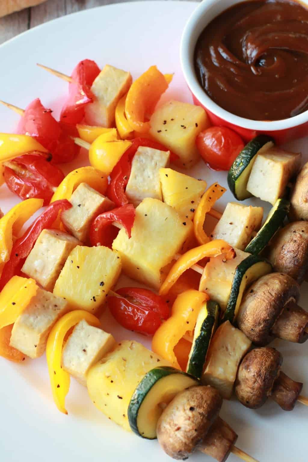 Brochettes de légumes sur une plaque blanche avec une sauce satay.