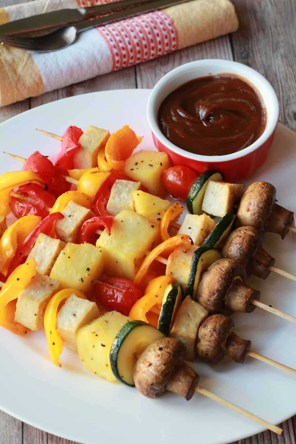 Brochettes de légumes sur une plaque blanche avec une sauce trempette satay.