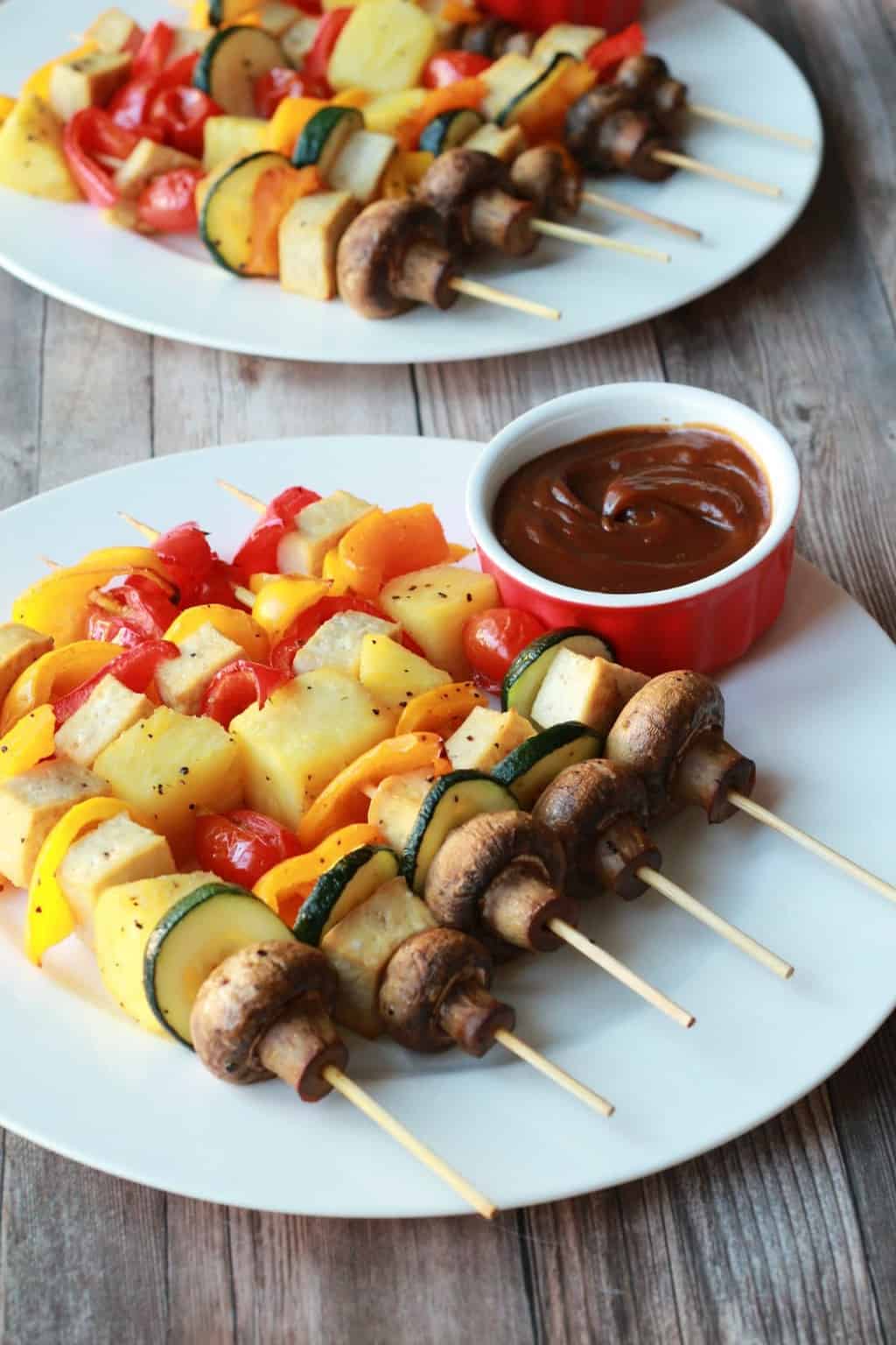Brochettes de légumes sur des assiettes blanches avec sauce satay.