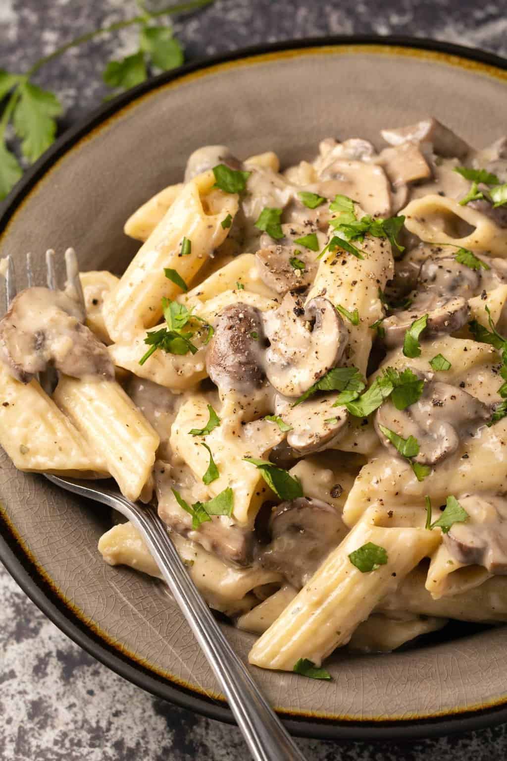 Pâtes aux champignons végétaliennes garnies de coriandre hachée dans un bol en pierre avec une fourchette.