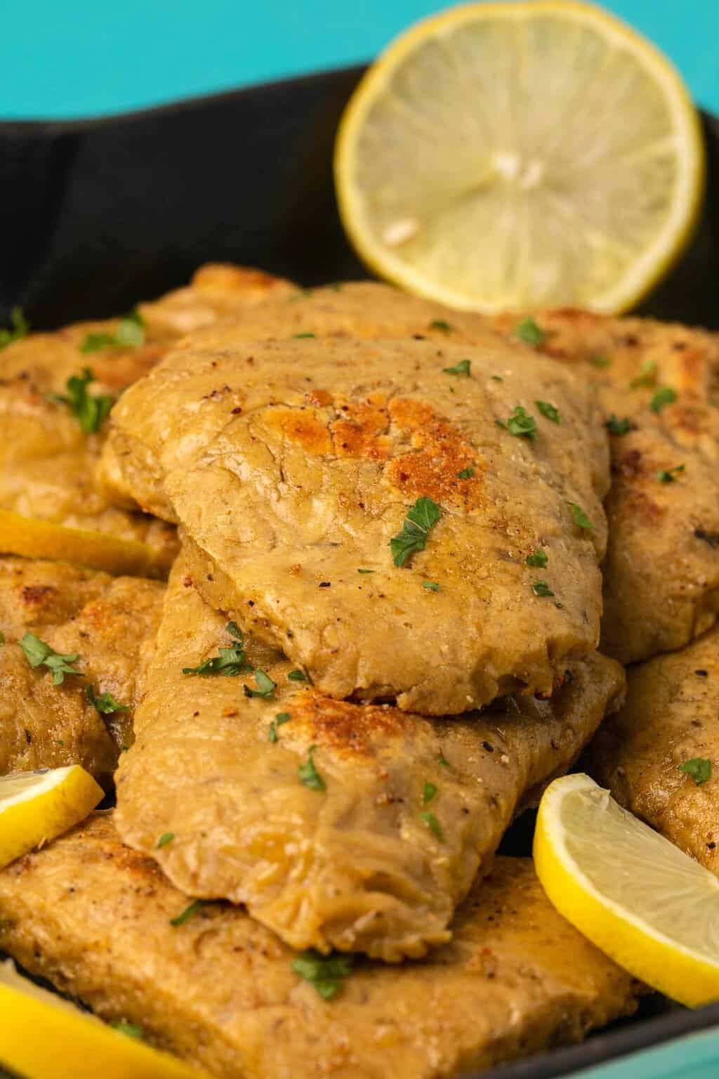 Filets de poulet végétaliens garnis de persil haché et de tranches de citron frais.