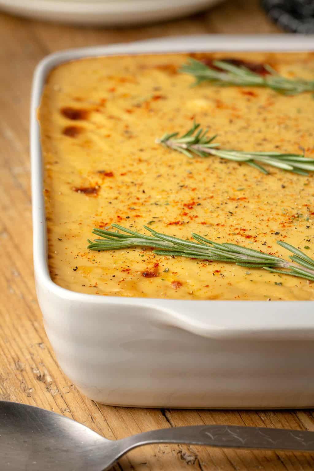Moussaka végétalienne garnie de romarin frais dans un plat de cuisson blanc.