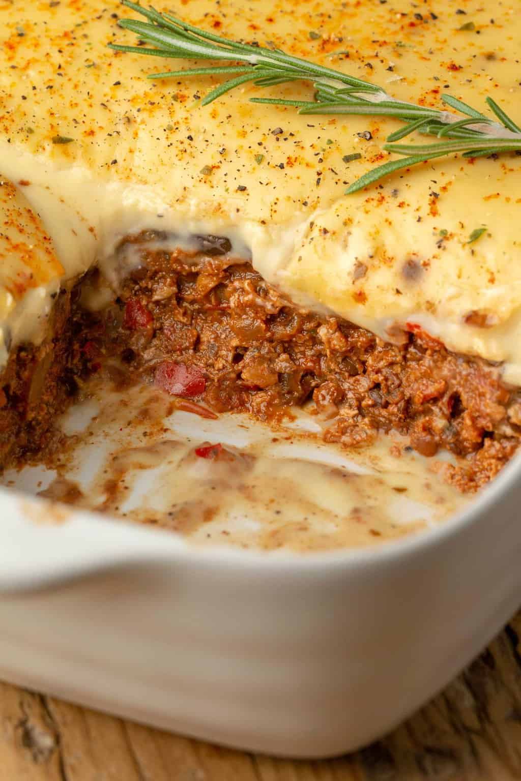 Moussaka végétalienne garnie d'un brin de romarin frais dans un plat de cuisson blanc.