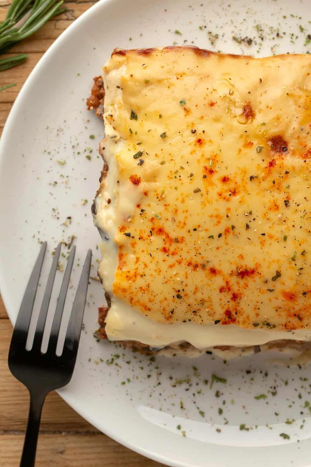 Une tranche de moussaka végétalienne sur une plaque blanche avec une fourchette.