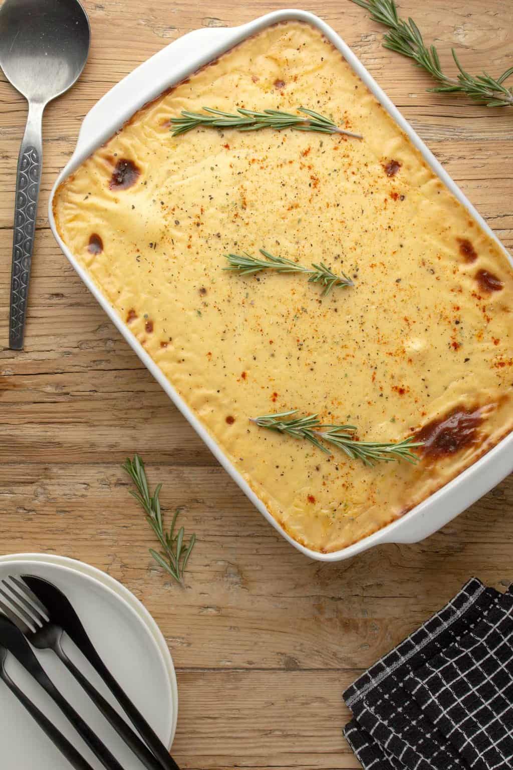Moussaka végétalienne garnie de romarin frais dans un plat de cuisson blanc.
