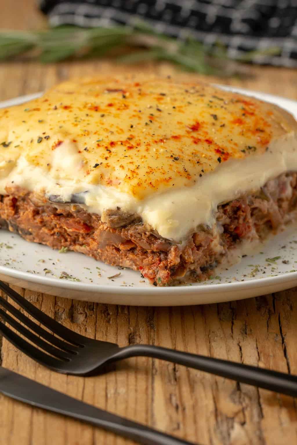 Une tranche de moussaka végétalienne sur une plaque blanche.