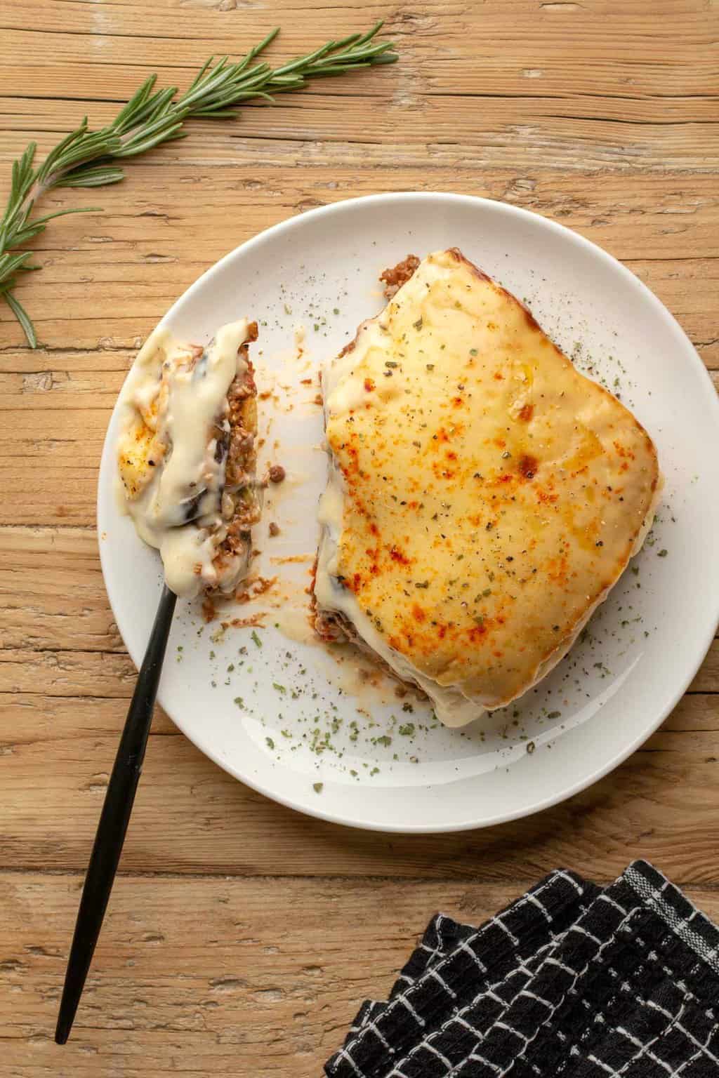 Une tranche de moussaka végétalienne sur une plaque blanche avec une fourchette.