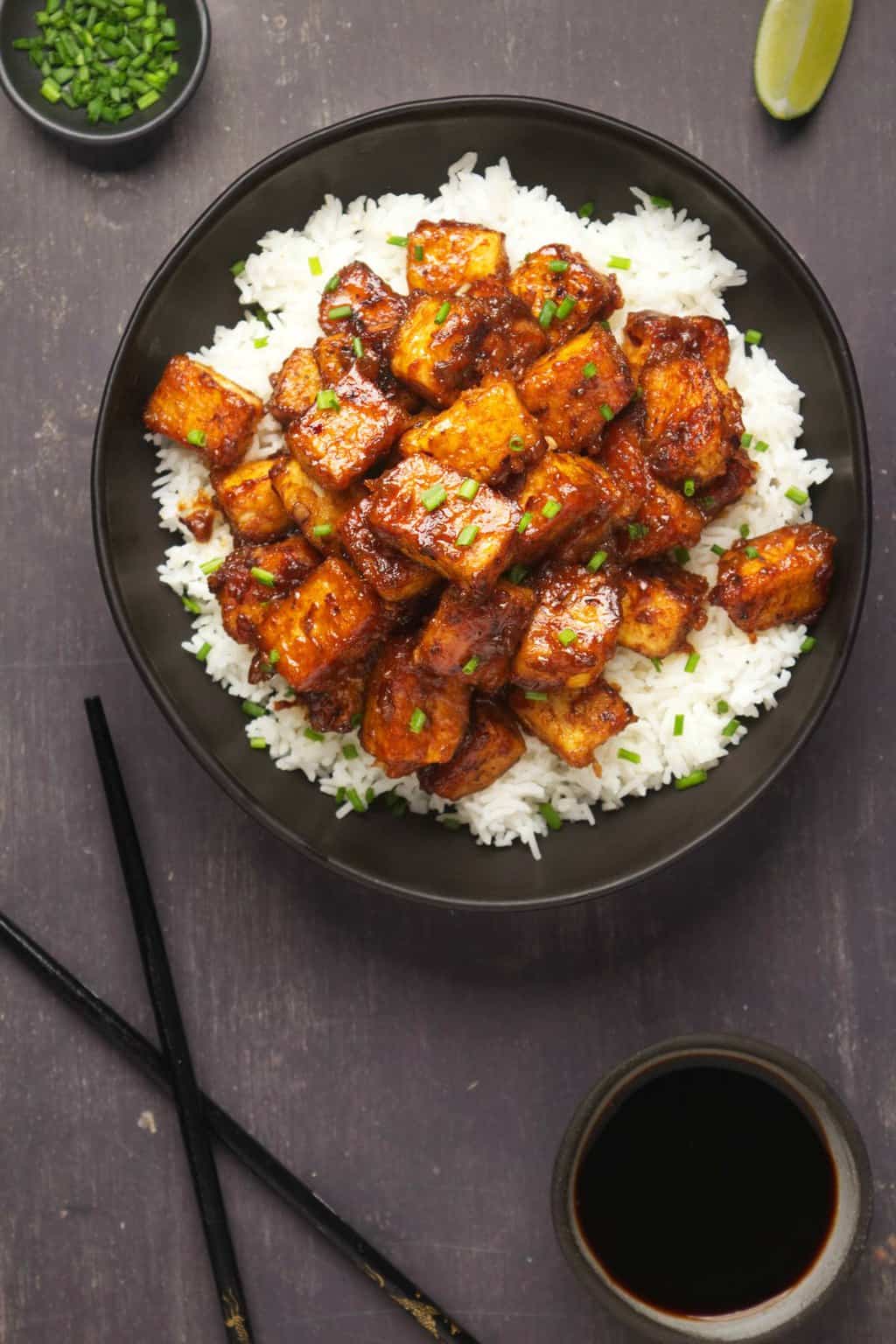 Tofu du Général Tso servi avec du riz basmati et de la ciboulette hachée dans un bol noir. 