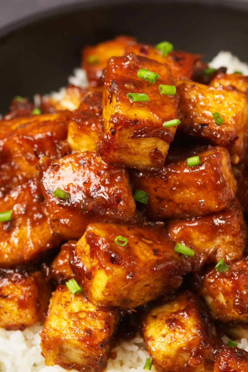 Tofu du Général Tso servi avec du riz basmati et de la ciboulette hachée dans un bol noir. 