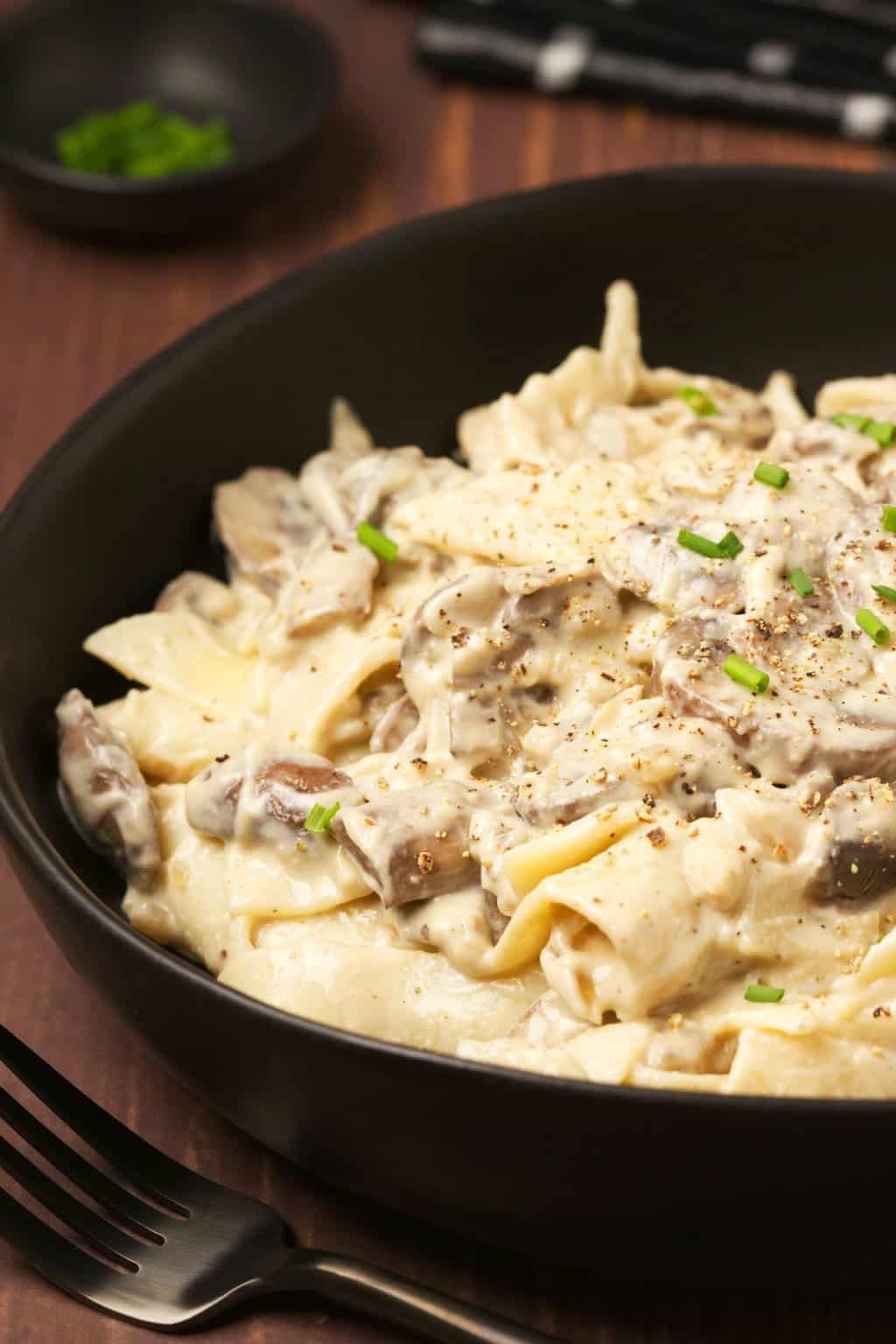 Stroganoff aux champignons végétalien garni de ciboulette hachée dans un bol noir.