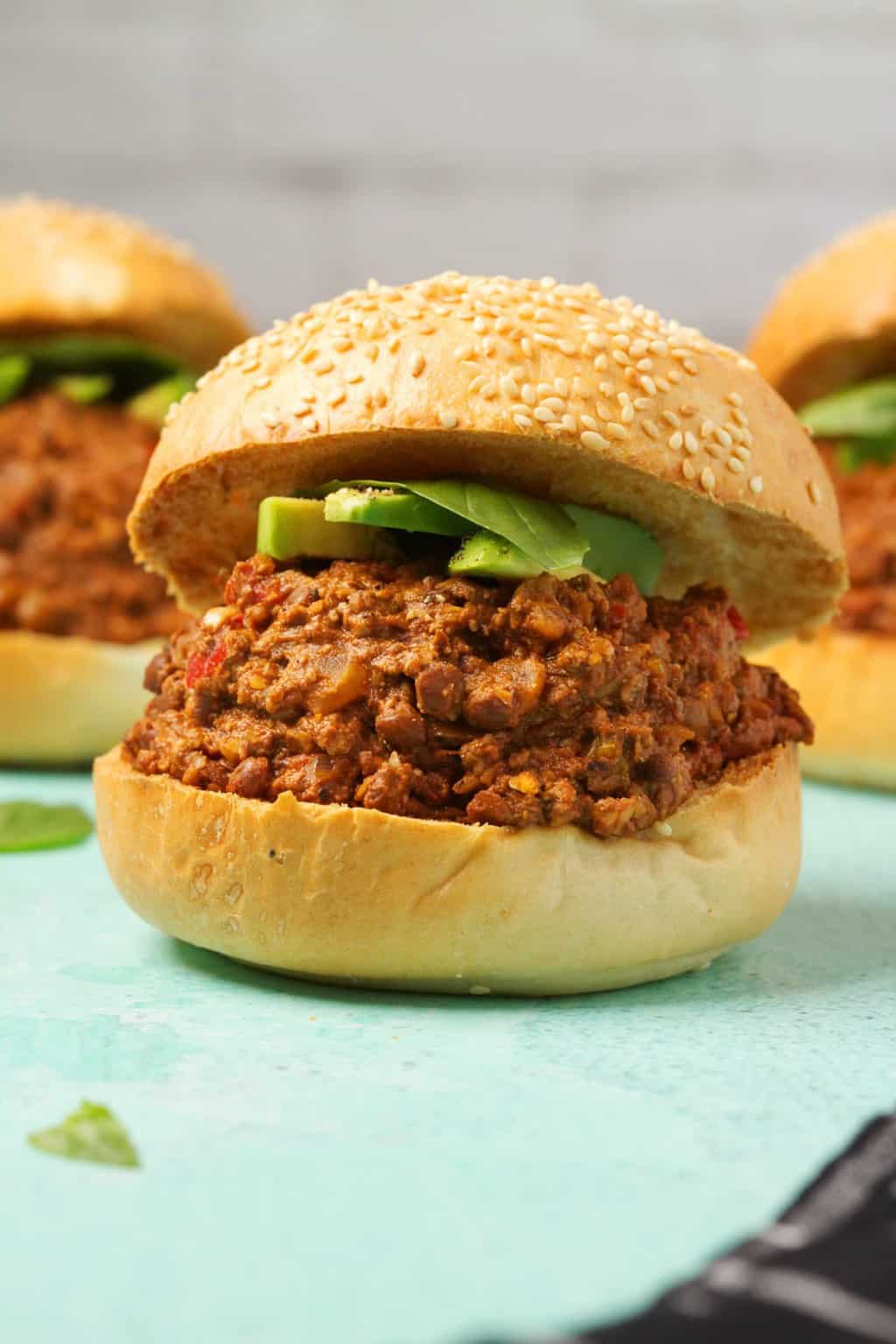Vegan Sloppy Joe avec de la viande hachée végétalienne maison et garni d'avocat en tranches et de feuilles de basilic frais. 