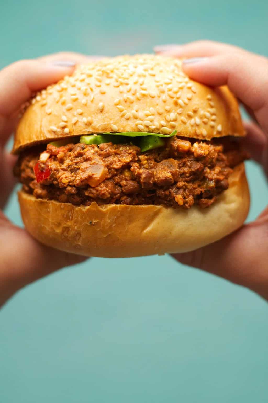 Tenant un Sloppy Joe végétalien dans les deux mains, prêt à prendre une bouchée. 