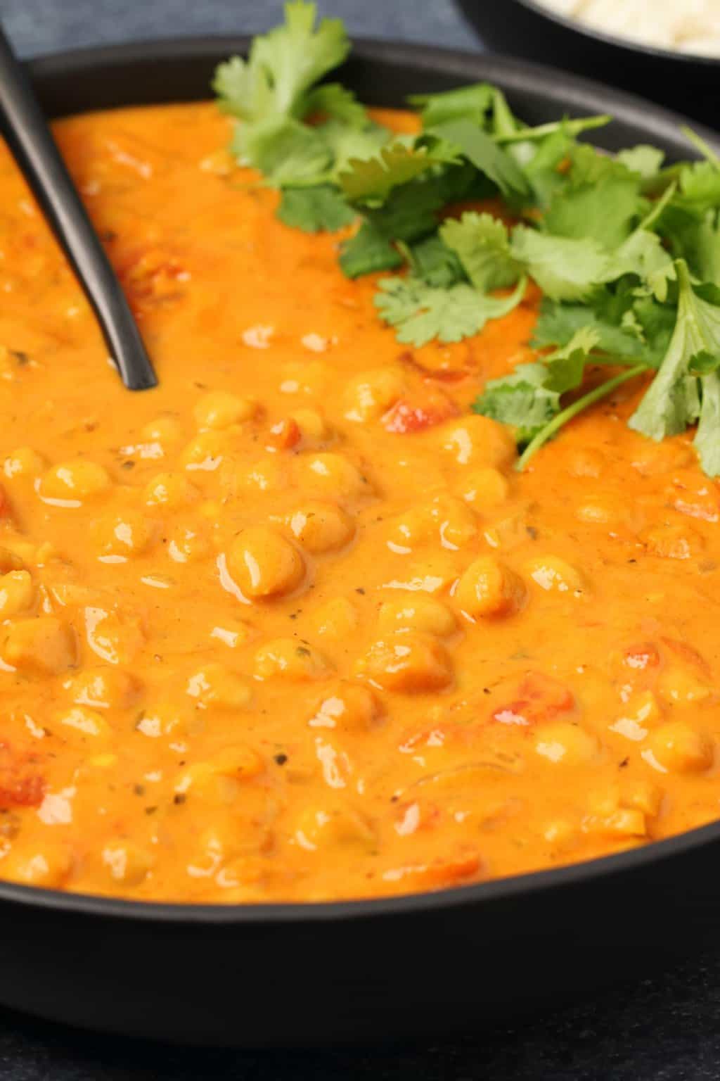 Curry de pois chiches végétalien garni de coriandre fraîche dans un bol noir avec une cuillère.