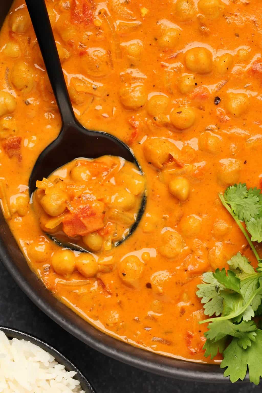 Curry de pois chiches garni de coriandre fraîche dans un bol noir avec une cuillère.