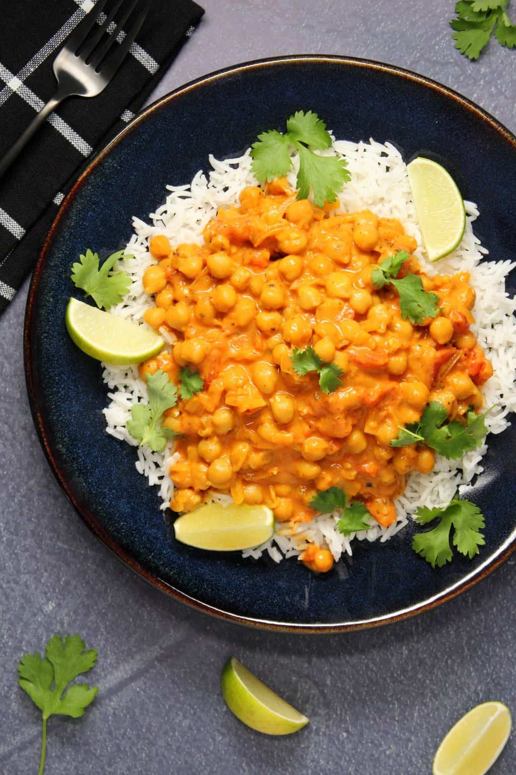 Curry de pois chiches végétalien avec riz basmati, coriandre fraîche et citron vert frais dans un bol noir.