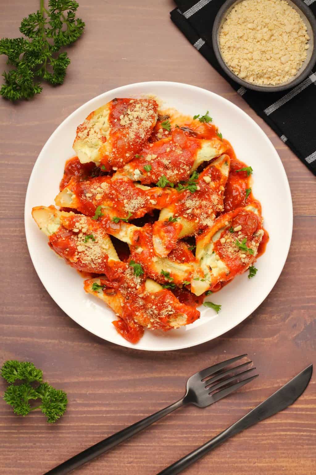 Coquilles farcies végétaliennes garnies de sauce marinara sur une plaque blanche.