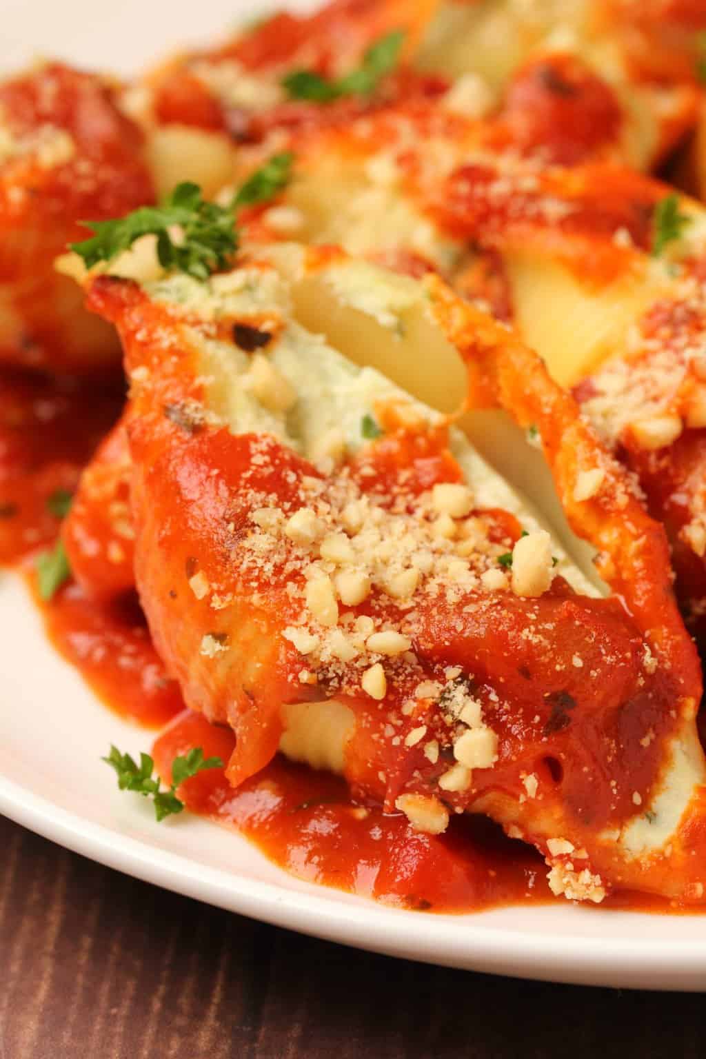 Coquilles farcies végétaliennes garnies de sauce marinara et de parmesan végétalien sur une plaque blanche.
