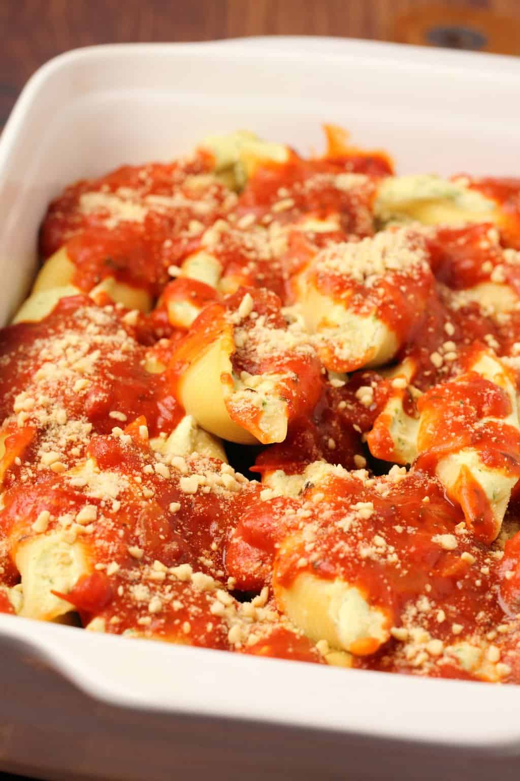 Coquilles farcies végétaliennes garnies de sauce marinara dans un plat de cuisson blanc.