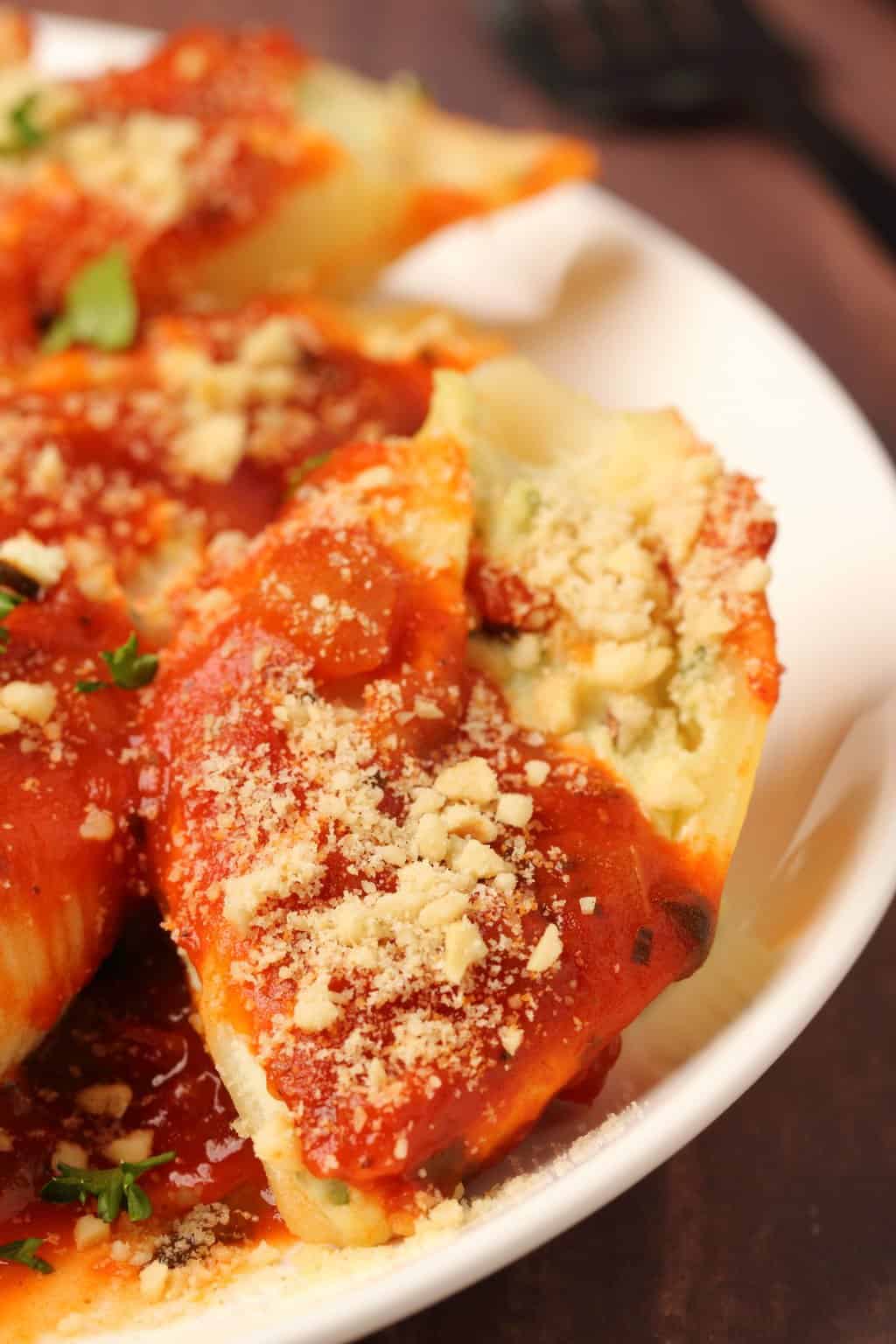 Coquilles farcies végétaliennes garnies de sauce marinara et de parmesan végétalien sur une plaque blanche.