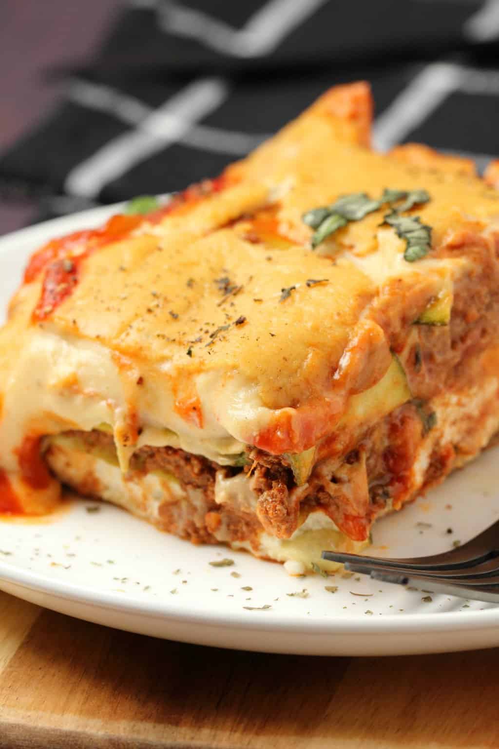 Une tranche de lasagne végétalienne sur une plaque blanche avec une fourchette. 