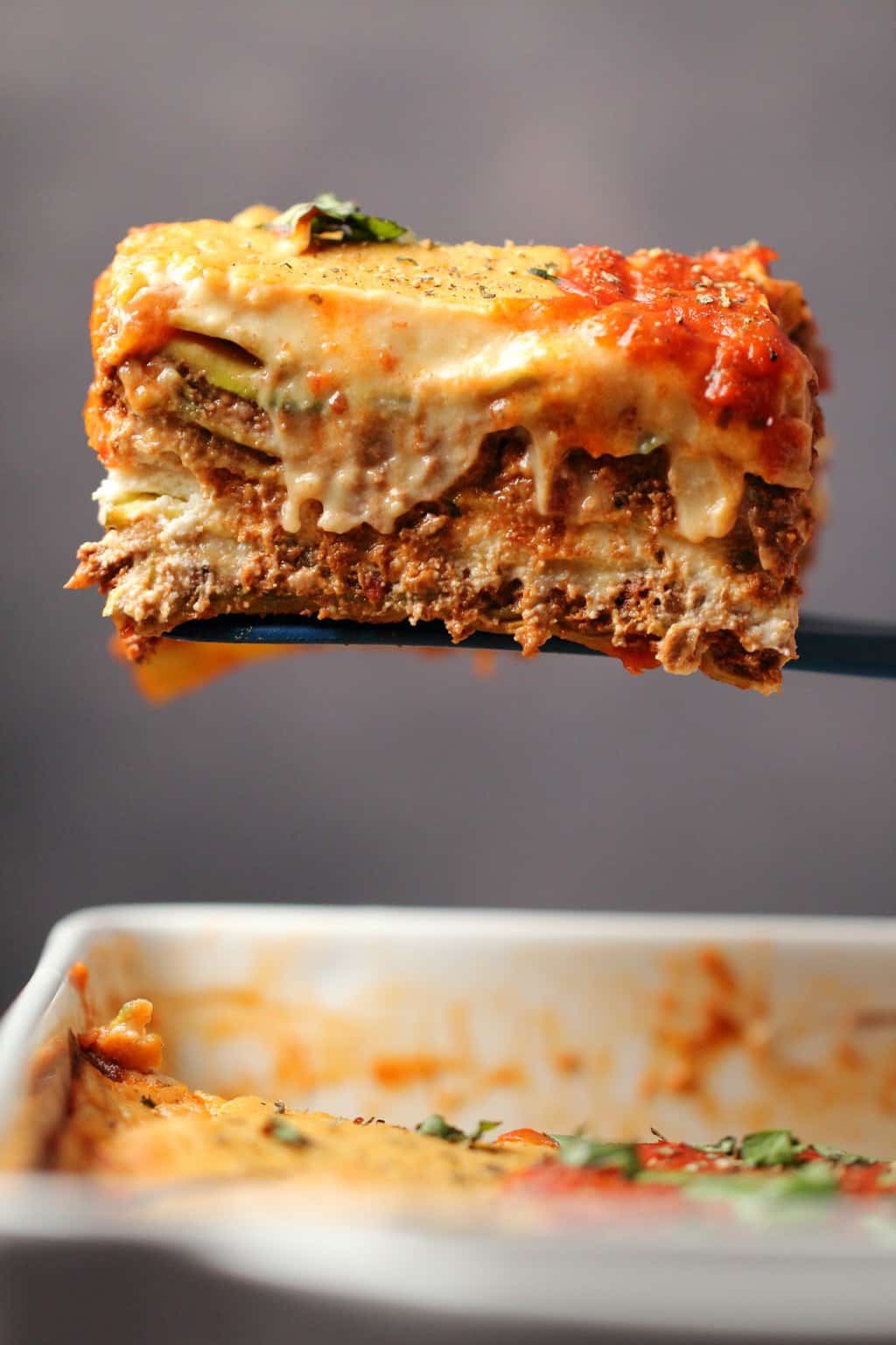 Une tranche de lasagne végétalienne sortant d'un plat blanc. 
