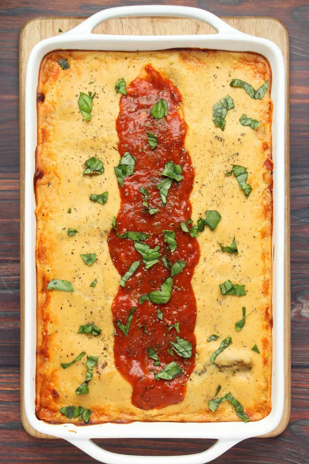 Lasagne végétalienne fraîchement cuite, décorée de sauce marinara et de basilic frais haché dans un plat blanc. 