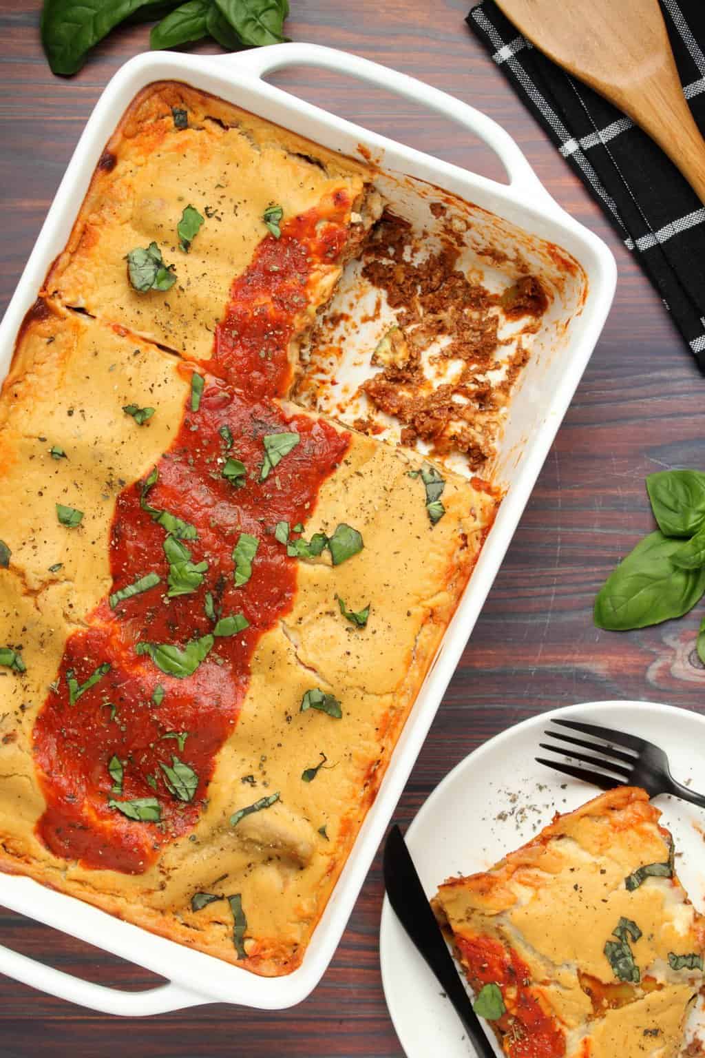 Lasagne végétalienne dans un plat blanc avec une tranche retirée. 