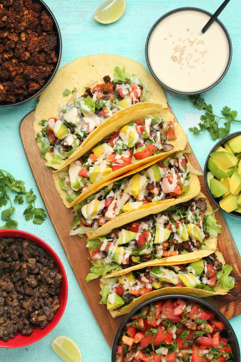 Tacos végétaliens aux haricots noirs, viande taco végétalienne, pico de gallo, avocat et sauce tahini sur une planche de bois. 