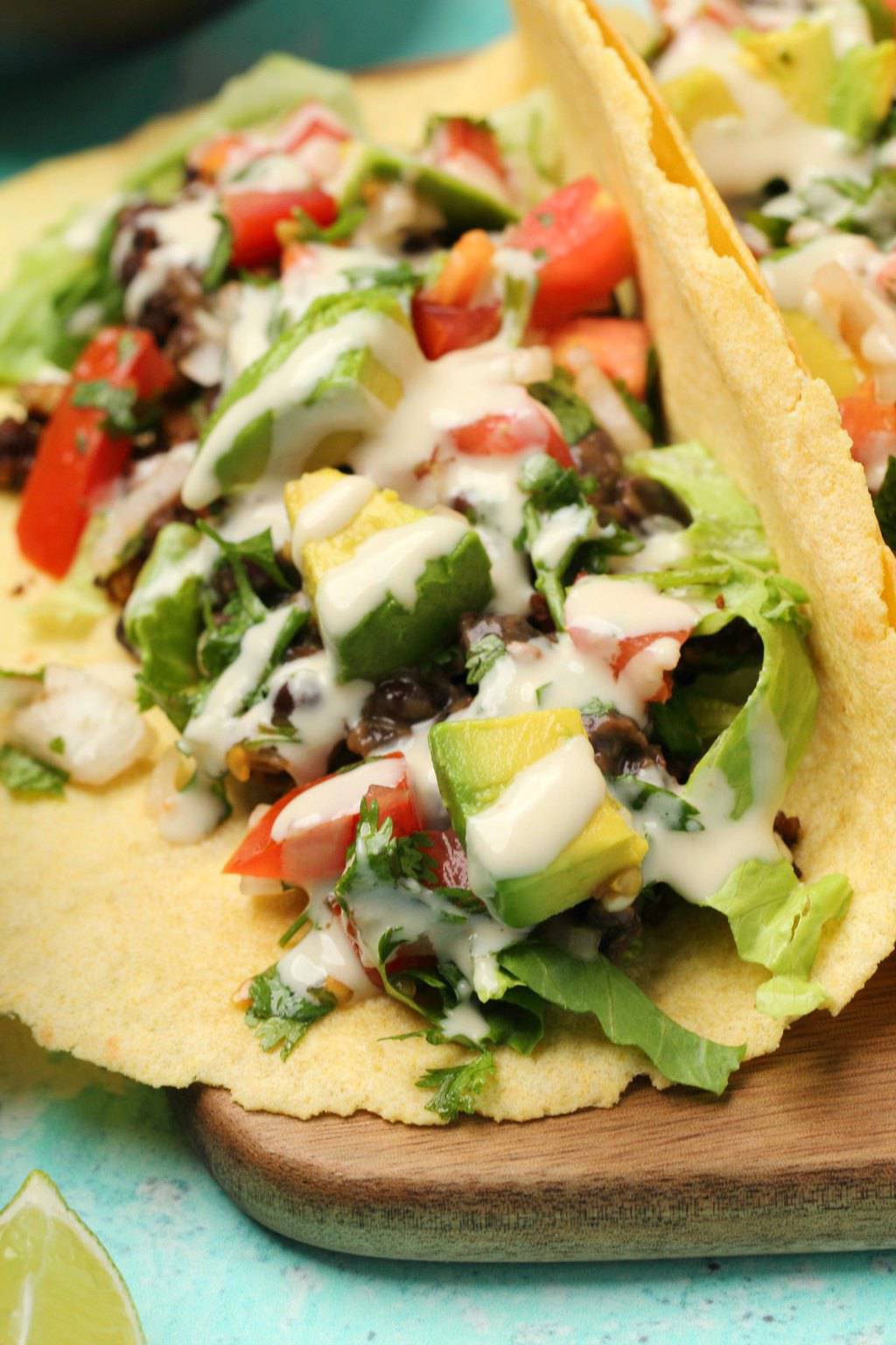 Tacos végétaliens farcis aux haricots noirs, viande taco végétalienne, pico de gallo, avocat et sauce tahini sur une planche de bois. 