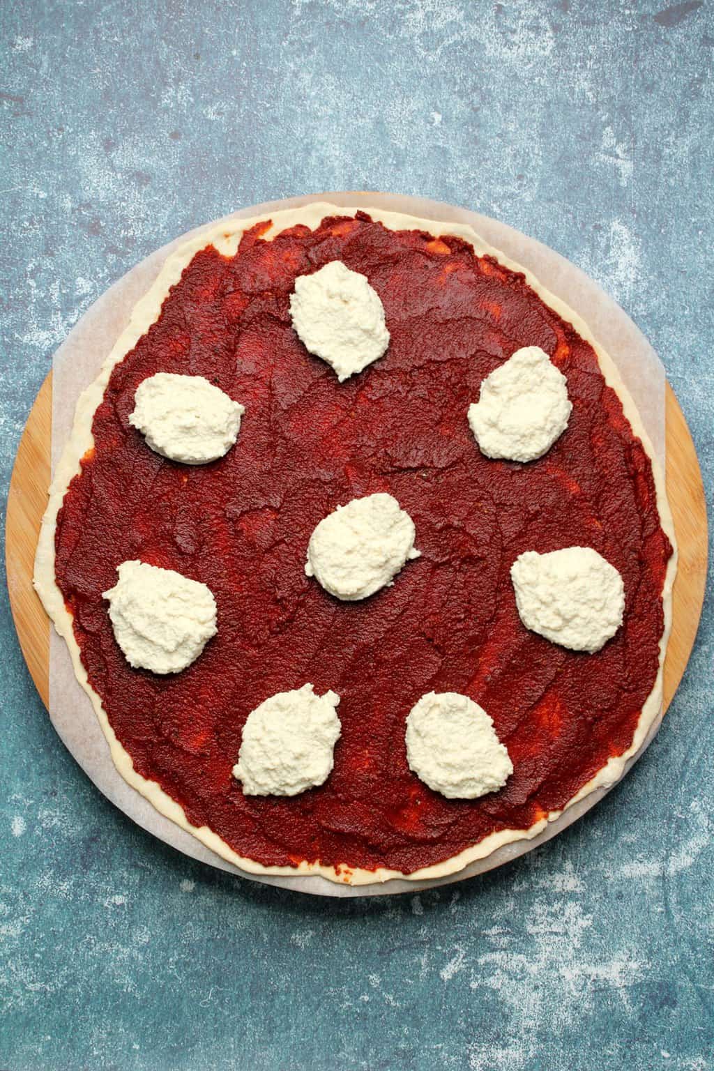 Base de pizza végétalienne non cuite avec sauce tomate et ricotta végétalienne. 