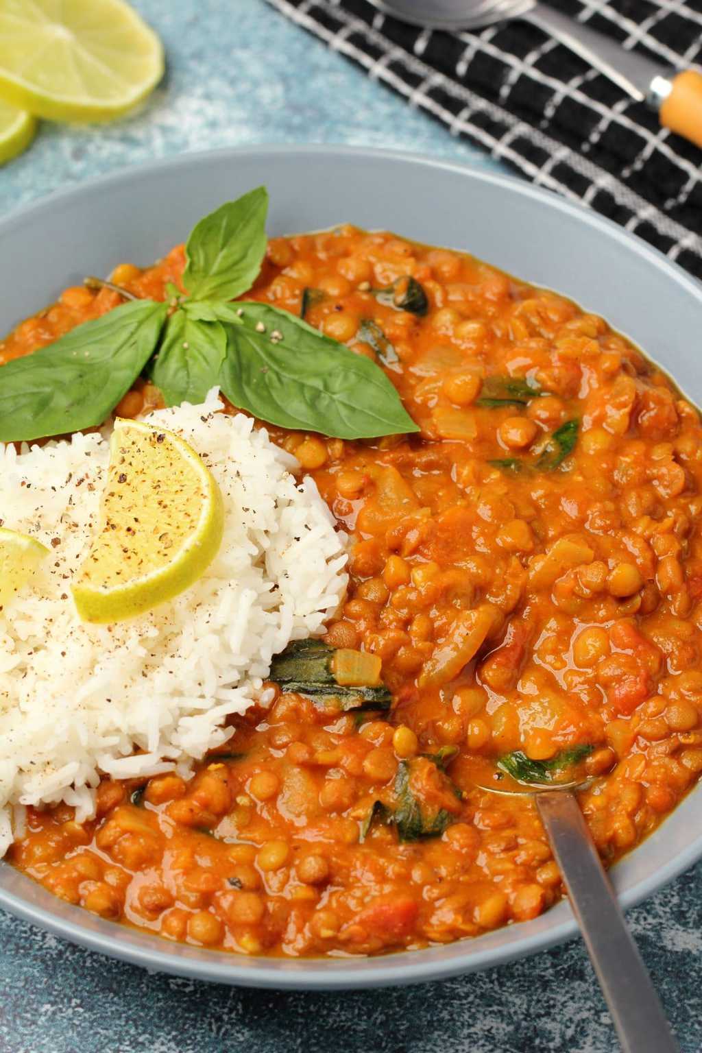 Curry de lentilles végétaliennes avec riz basmati et basilic frais dans un bol bleu.