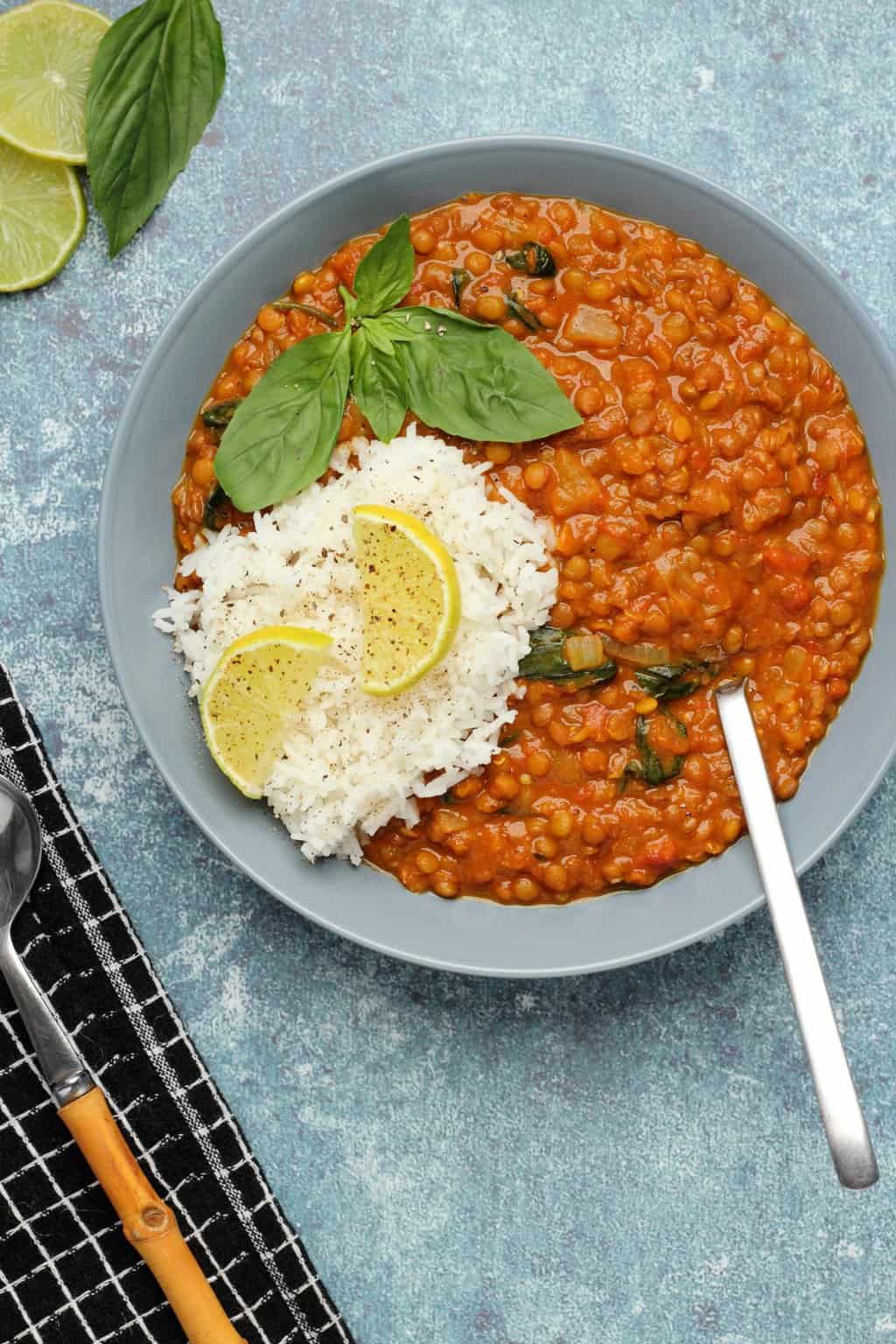 Curry de lentilles végétaliennes avec riz basmati et basilic frais dans un bol bleu.