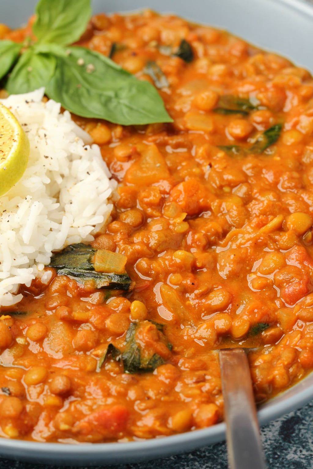 Curry de lentilles végétaliennes avec riz basmati et basilic frais dans un bol bleu.