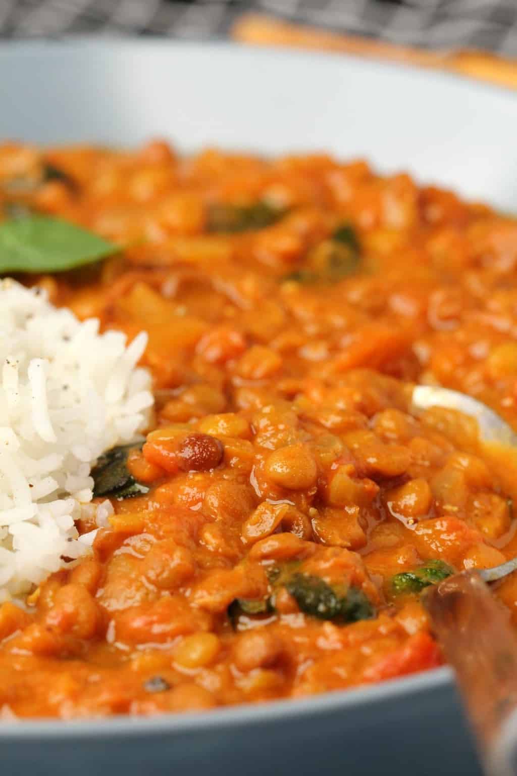 Curry de lentilles végétaliennes avec du riz basmati dans un bol bleu avec une cuillère.