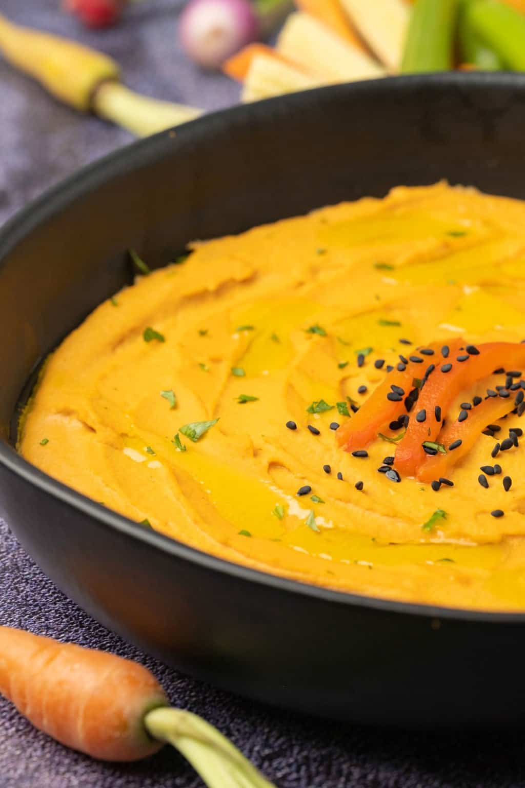 Houmous de poivron rouge rôti garni de graines de sésame dans un bol noir.