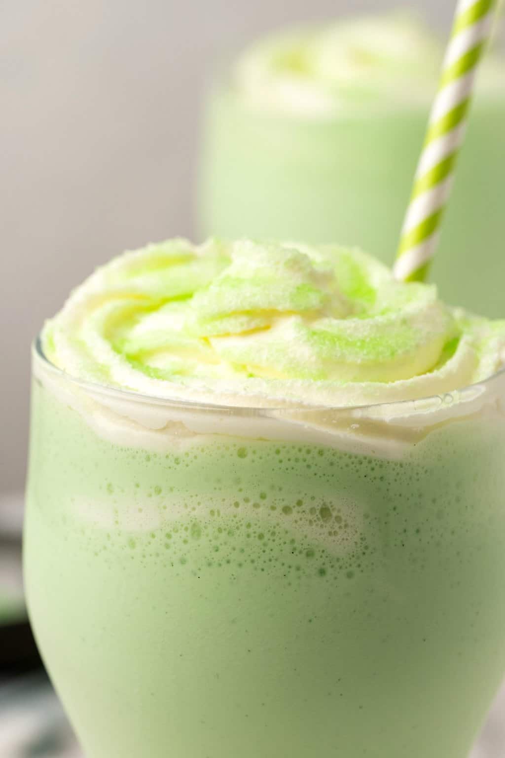 Shake de shamrock végétalien dans un grand verre de crème fouettée et de sucre à poncer vert.