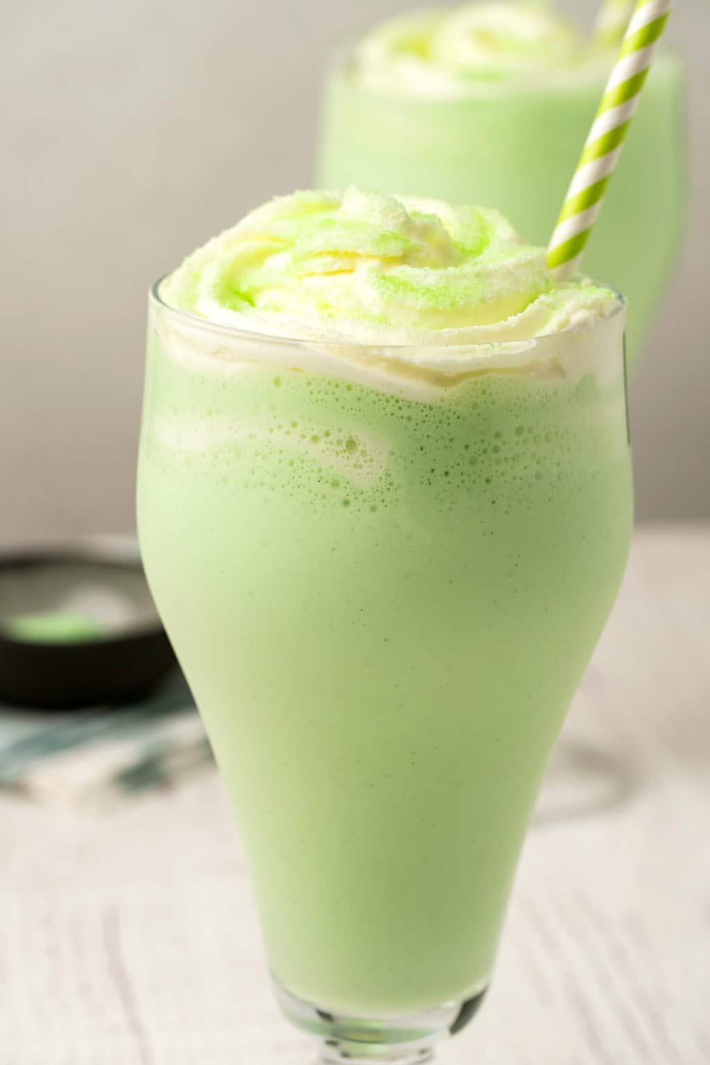 Shake de shamrock végétalien dans un grand verre garni de crème fouettée et de sucre à poncer vert.