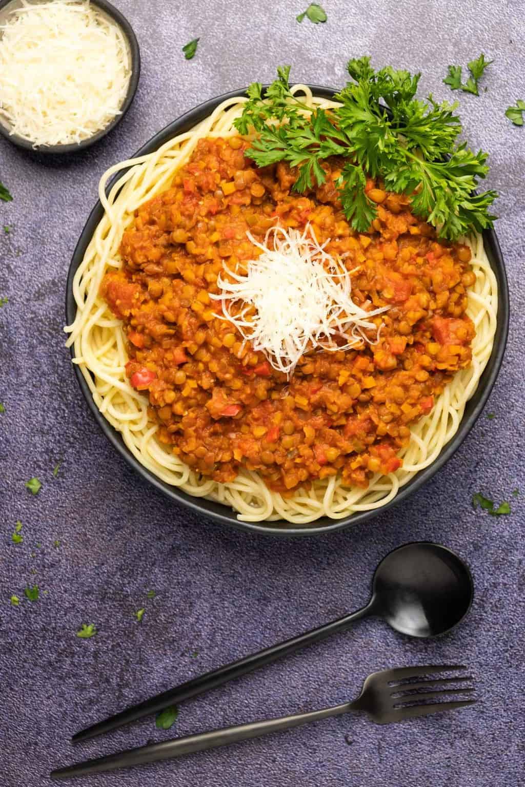 Bolognaise aux lentilles garnie de parmesan végétalien dans un bol noir.