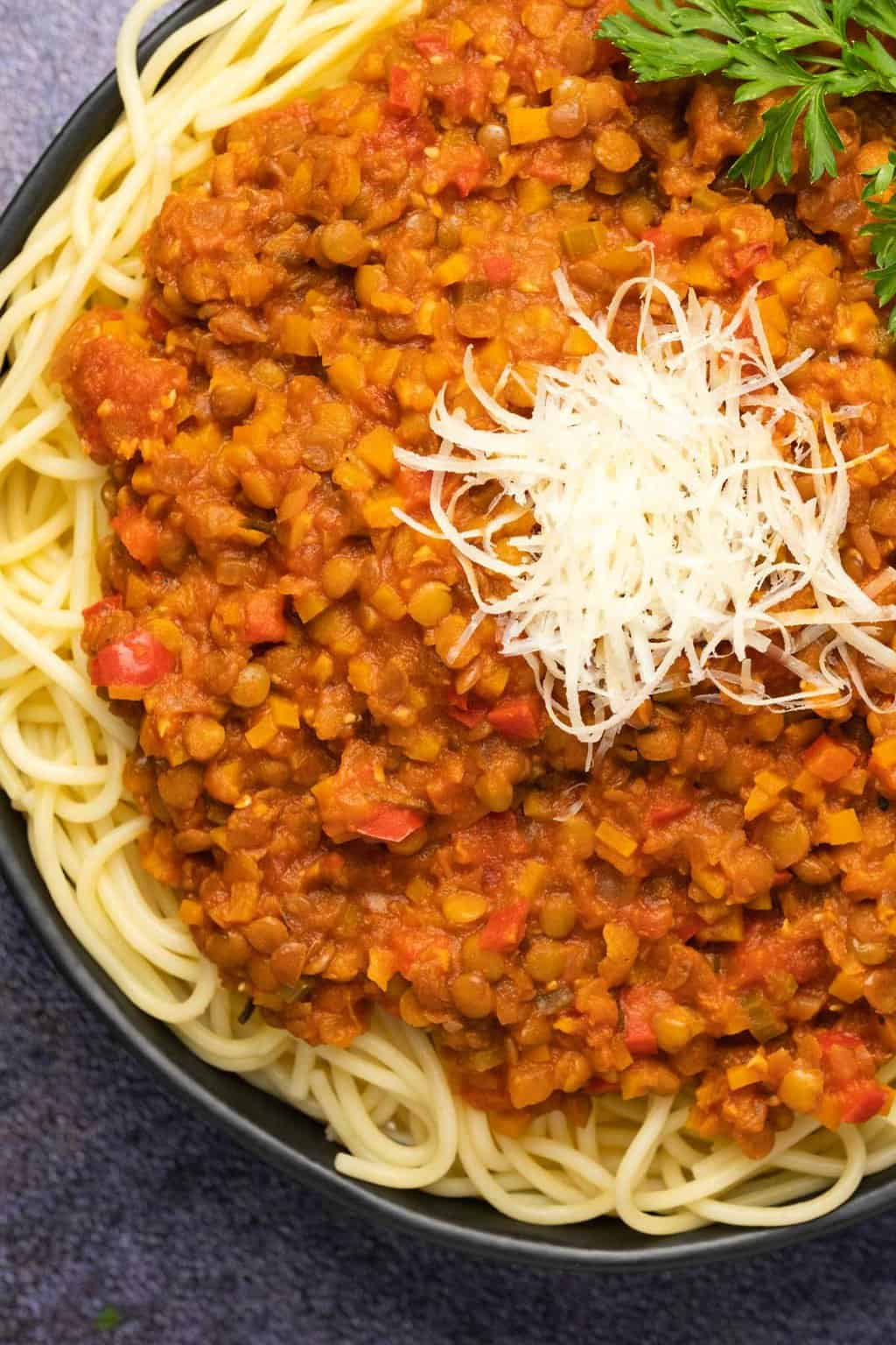 Bolognaise aux lentilles garnie de parmesan végétalien et de persil dans un bol noir.