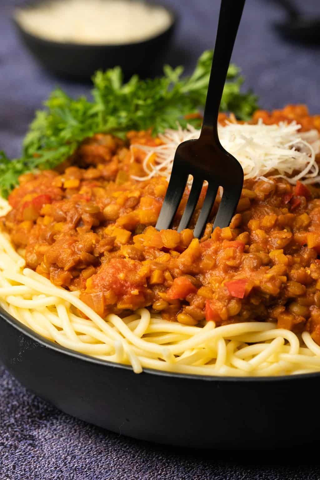 Bolognaise aux lentilles sur des spaghettis dans un bol noir avec une fourchette.