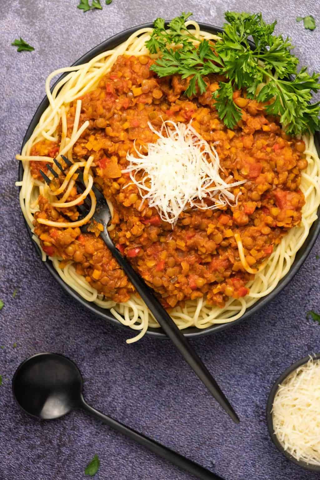 Bolognaise aux lentilles avec spaghetti et parmesan végétalien dans un bol noir.