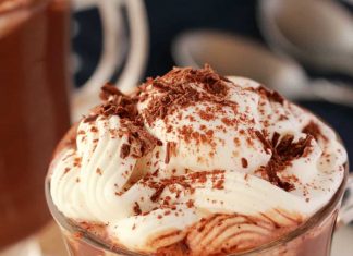 Chocolat chaud végétalien – Loving It Vegan Chocolat chaud végétalien dans une tasse en verre garnie de crème fouettée et de copeaux de chocolat.