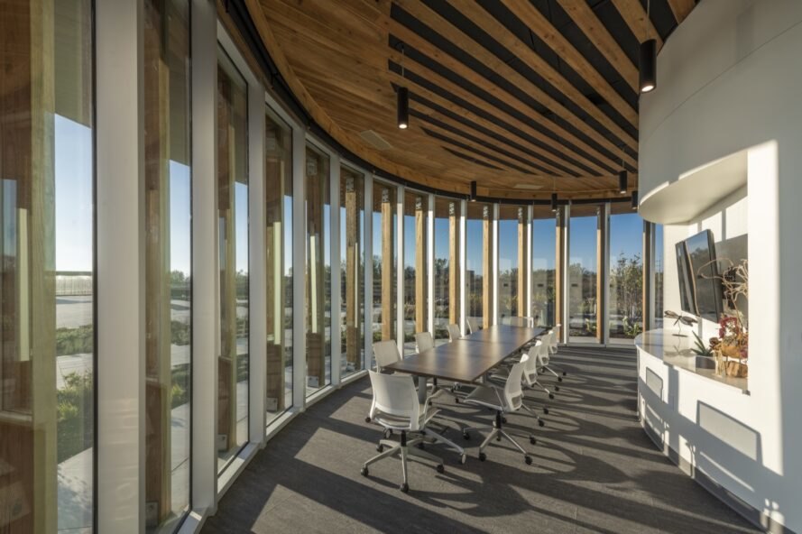 bureau avec des chaises de bureau blanches près d'un mur incurvé de fenêtres à ossature de bois