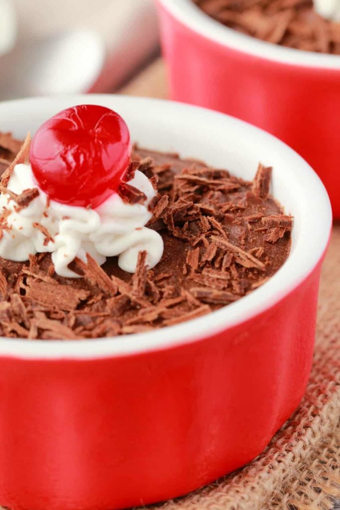 Mousse au chocolat végétalienne dans un ramequin rouge et blanc avec des copeaux de chocolat, une cuillerée de crème de noix de coco et une cerise