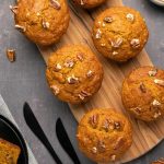 Muffins citrouilles végétaliens – Loving It Vegan Muffins citrouilles végétaliens garnis de pacanes hachées sur une planche de bois.