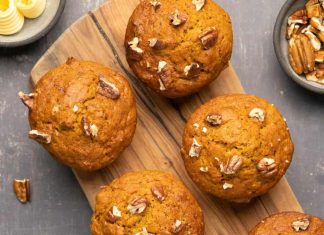 Muffins citrouilles végétaliens – Loving It Vegan Muffins citrouilles végétaliens garnis de pacanes hachées sur une planche de bois.