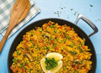 Paella végétalienne – Recette vegan Paella végétalienne garnie de quartiers de citron et de persil haché dans une poêle à paella noire.