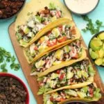 Tacos végétaliens – Lilypop Tacos végétaliens aux haricots noirs, viande taco végétalienne, pico de gallo, avocat et sauce tahini sur une planche de bois.