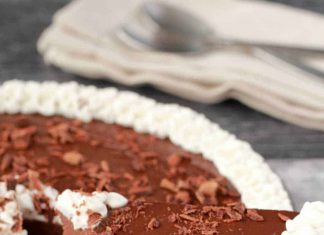 Tarte au chocolat végétalienne (sans cuisson) Tarte au chocolat végétalienne décorée de crème de noix de coco fouettée et de flocons de chocolat dans un plat à tarte en verre.