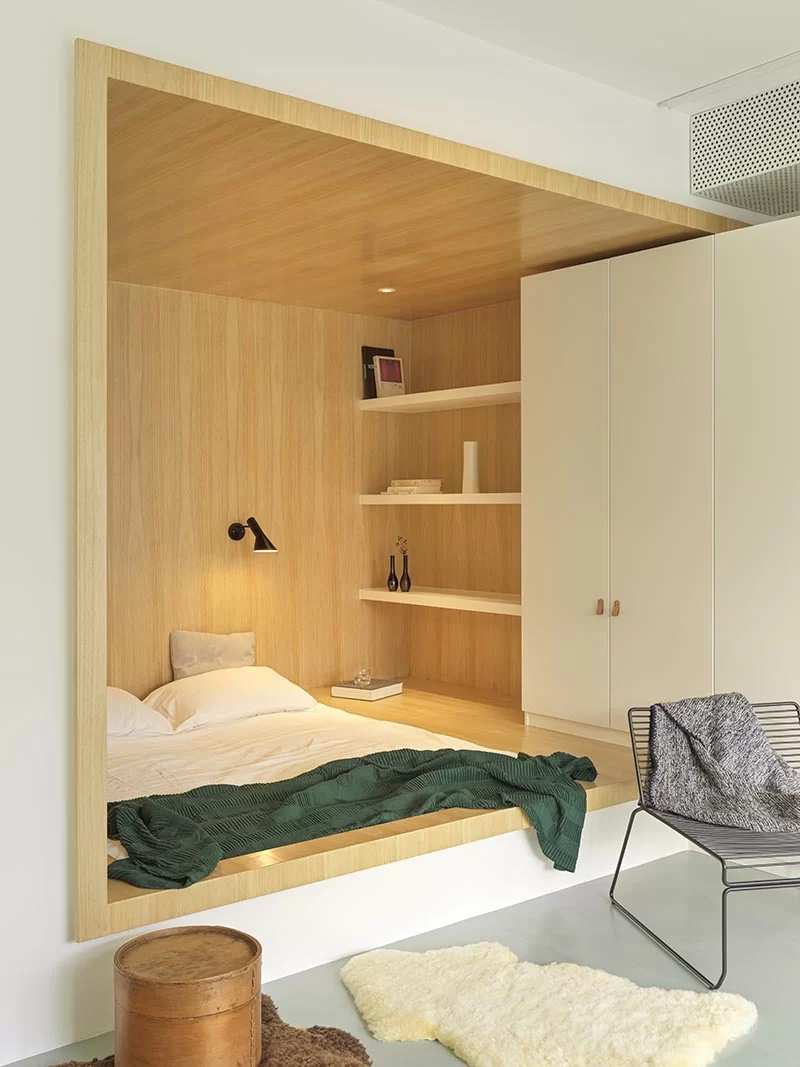 Au lieu d'avoir un lit autoportant, les concepteurs ont utilisé un petit coin de forme étrange positionné le lit dans la base de sa propre niche bordée de bois, permettant plus d'espace au sol grâce aux grandes fenêtres. #BedroomIdea #BedNook #BedNiche #BuiltInBed #InteriorDesign #ModernBedroom